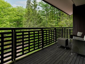 A wooden deck with a black railing, a wicker sofa, and a view of a forest. - Wan Wan Paradise Takayama (Takayama)