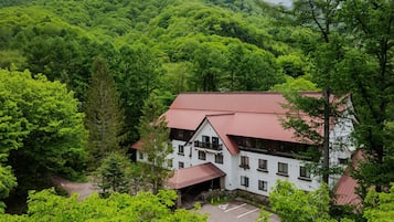A two-story building with a red roof, surrounded by dense green forest.