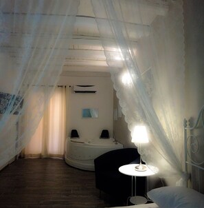 Una habitación con cama, mesita de noche con lámpara, una pequeña mesa redonda y baño con bañera y lavamanos.