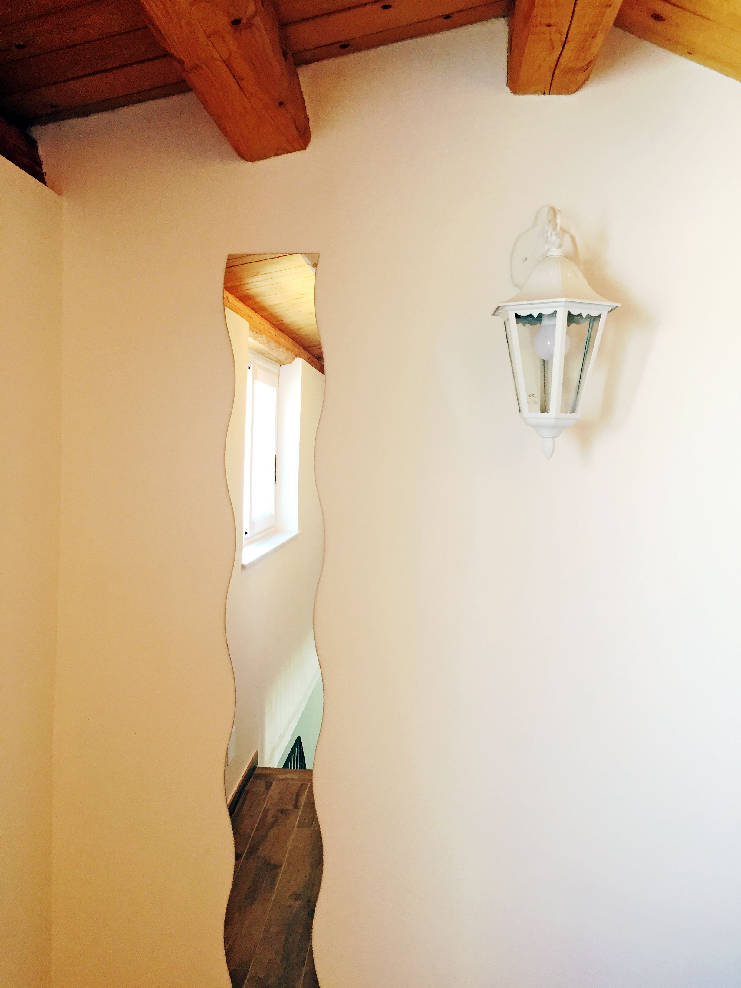 A hallway with a wooden ceiling, a white wall, and a white wall-mounted light fixture.
