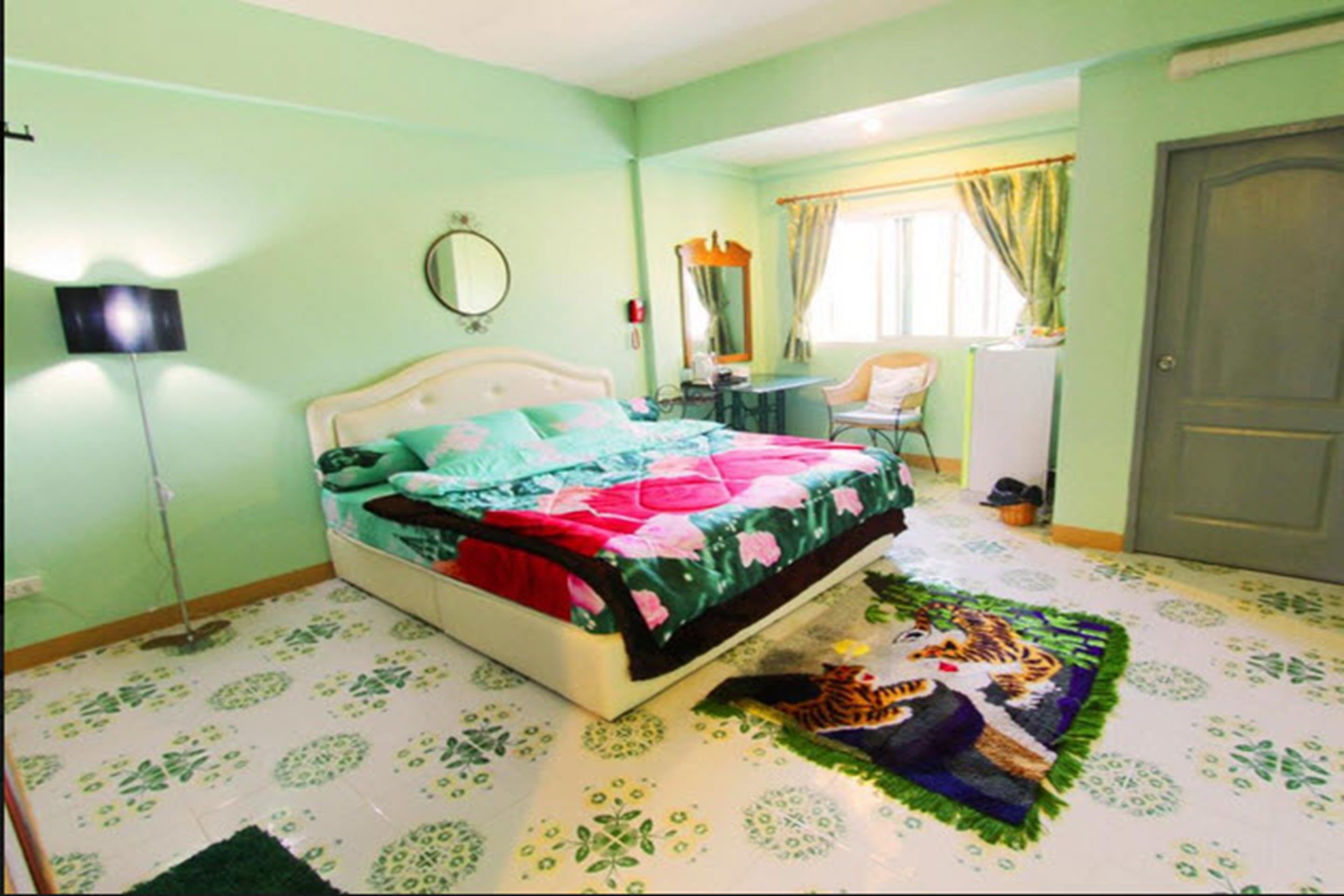A bedroom with a bed, a desk, a chair, a mirror, and a door.