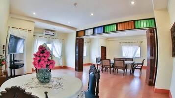 Una habitación amplia con zona de comedor, un jarrón grande de flores y un televisor.