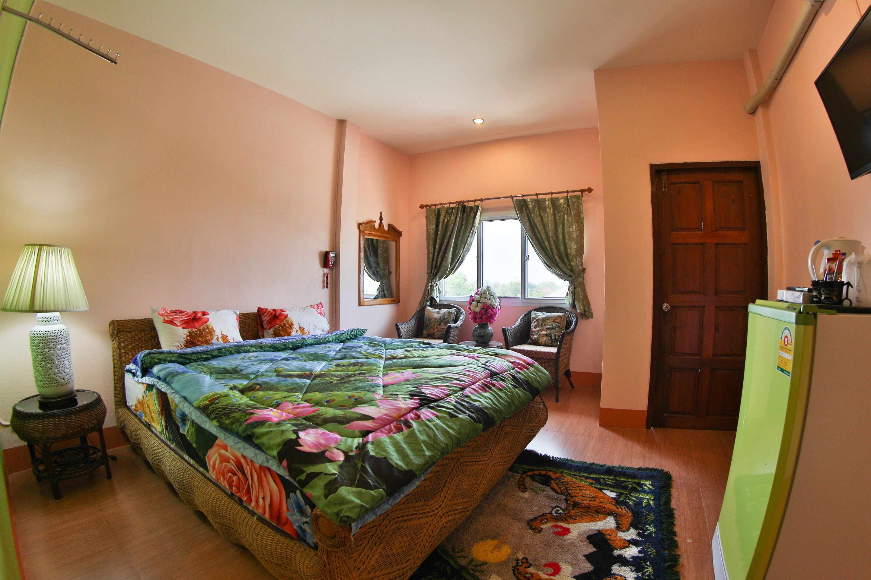 A bedroom with a bed, a nightstand, a lamp, a chair, a window with curtains, a door, and a refrigerator.