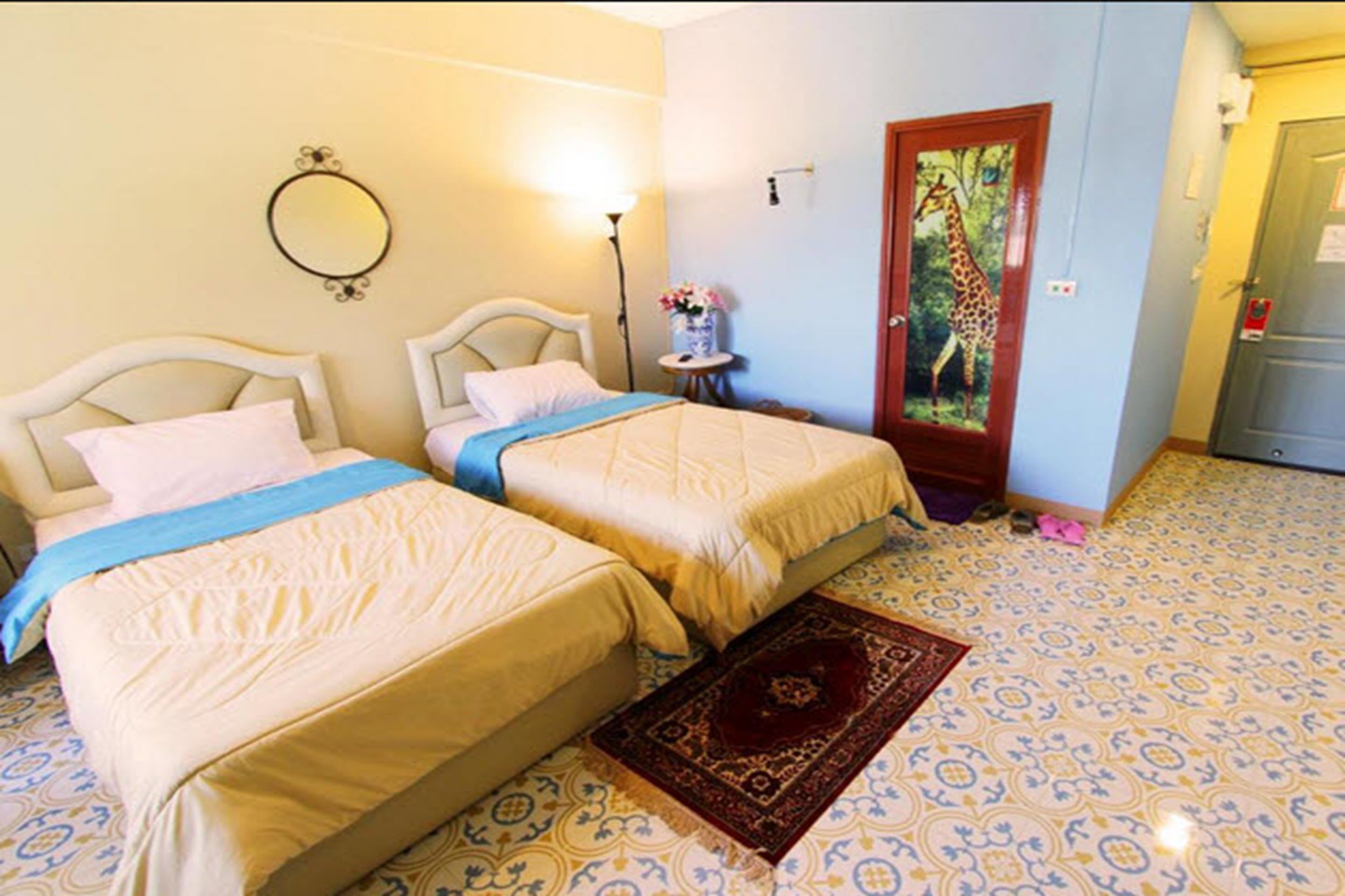 Una habitación con dos camas, un espejo, una puerta decorada con un cuadro de jirafa y suelo estampado.
