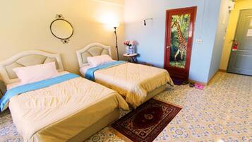 Una habitación con dos camas, un espejo, una puerta decorada con un cuadro de jirafa y suelo estampado.