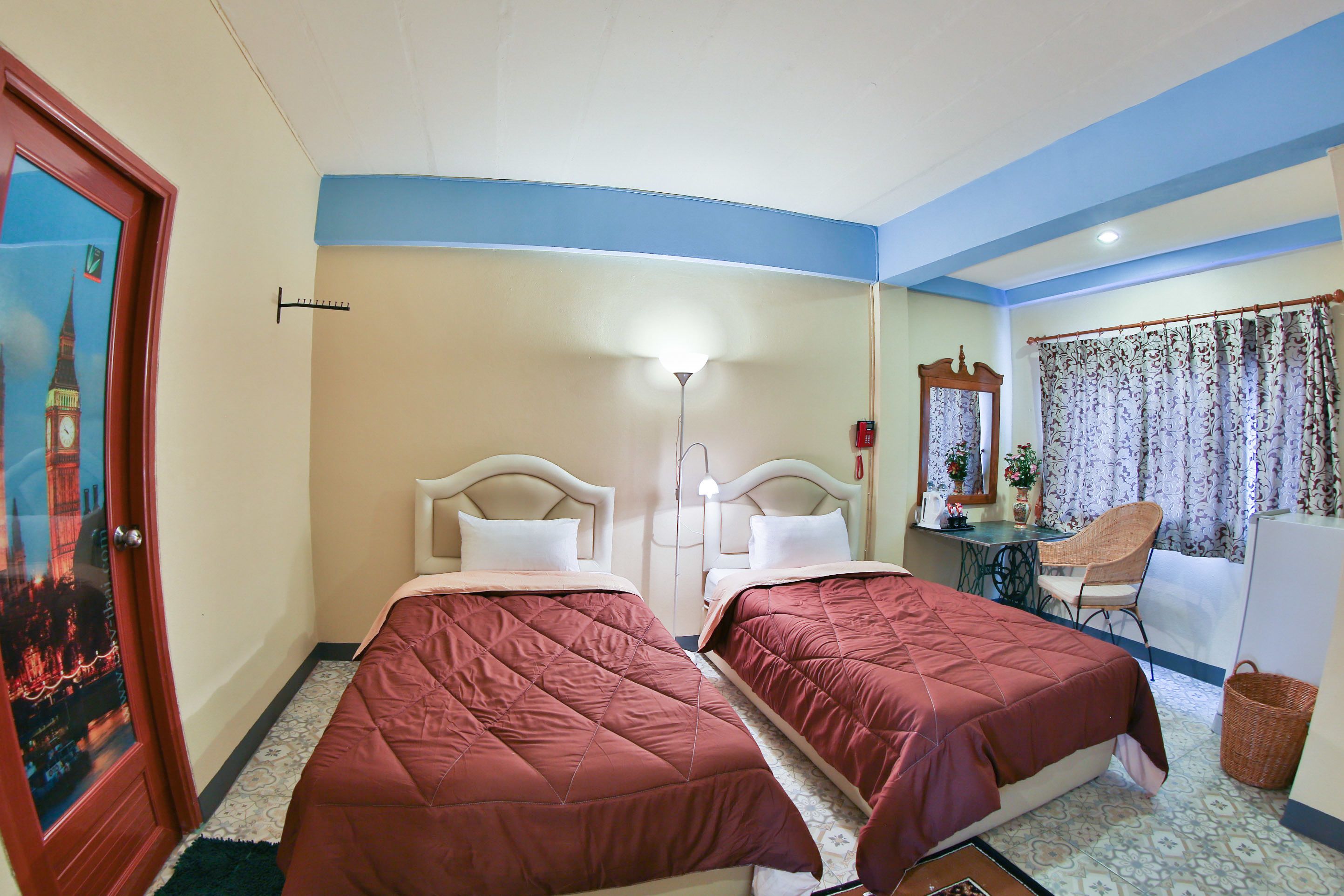 A hotel room with two beds, a desk, a chair, a lamp, and a window with a view of a clock tower.