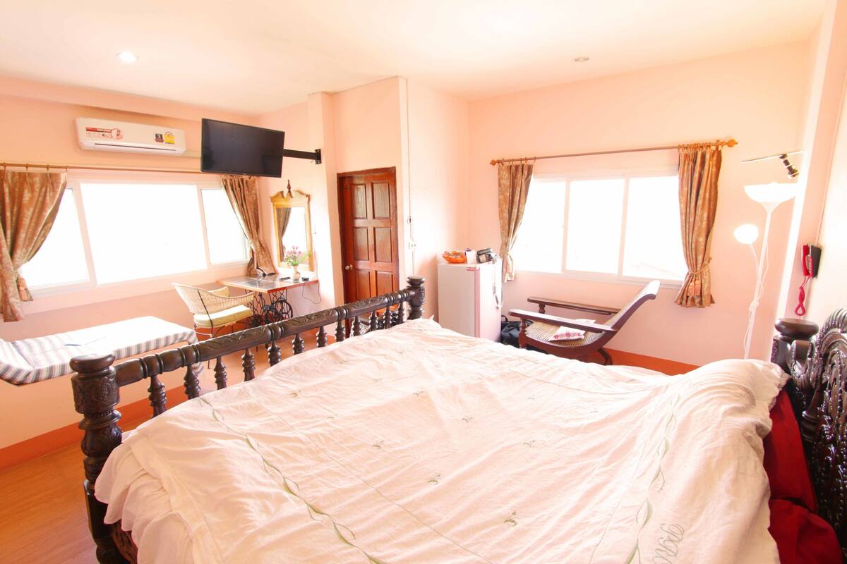 A bedroom with a bed, a television, an air conditioner, a desk, and a chair.