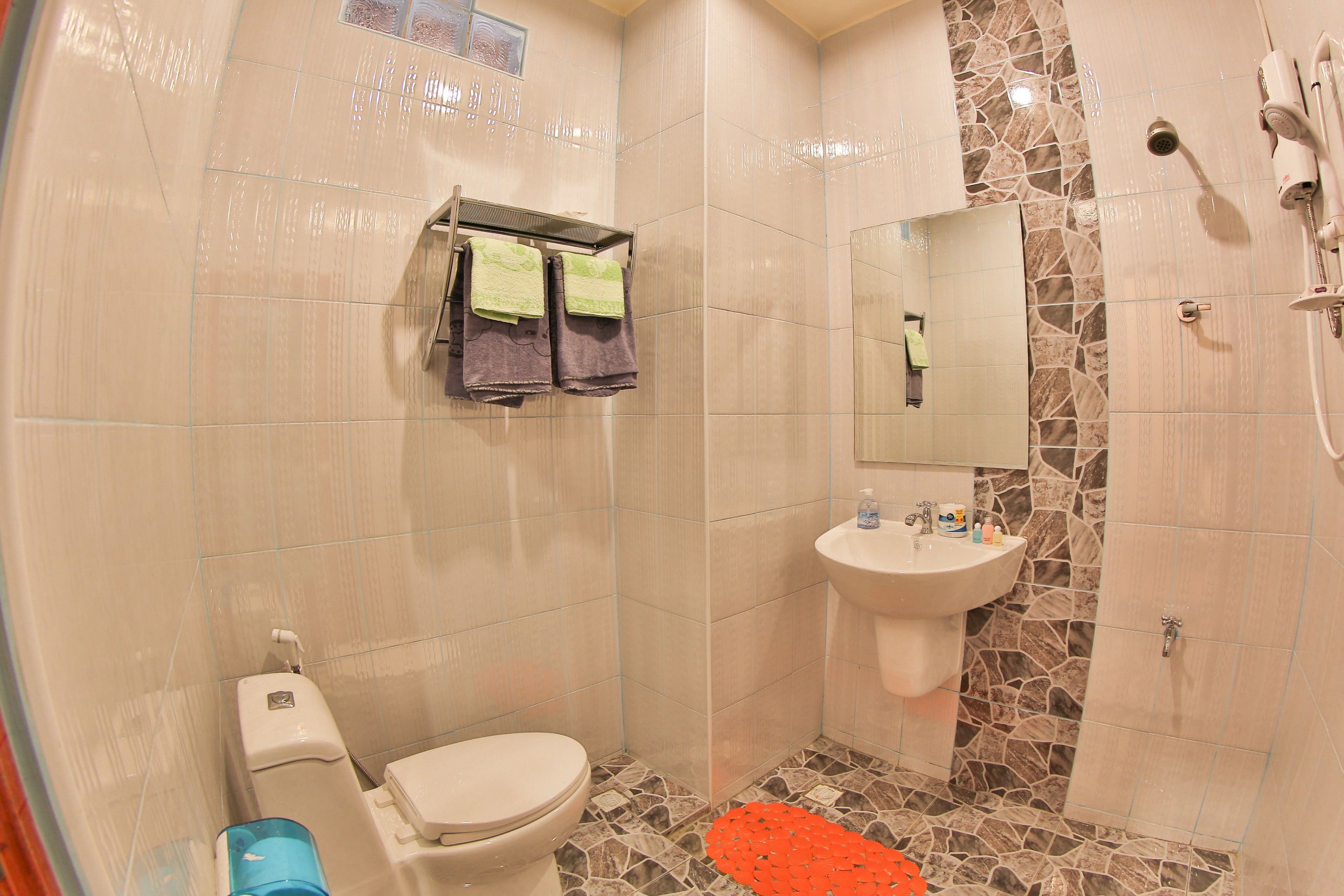 Une salle de bain avec des toilettes, un lavabo et une douche. Des serviettes sont suspendues sur un porte-serviettes et un miroir est placé au-dessus du lavabo.