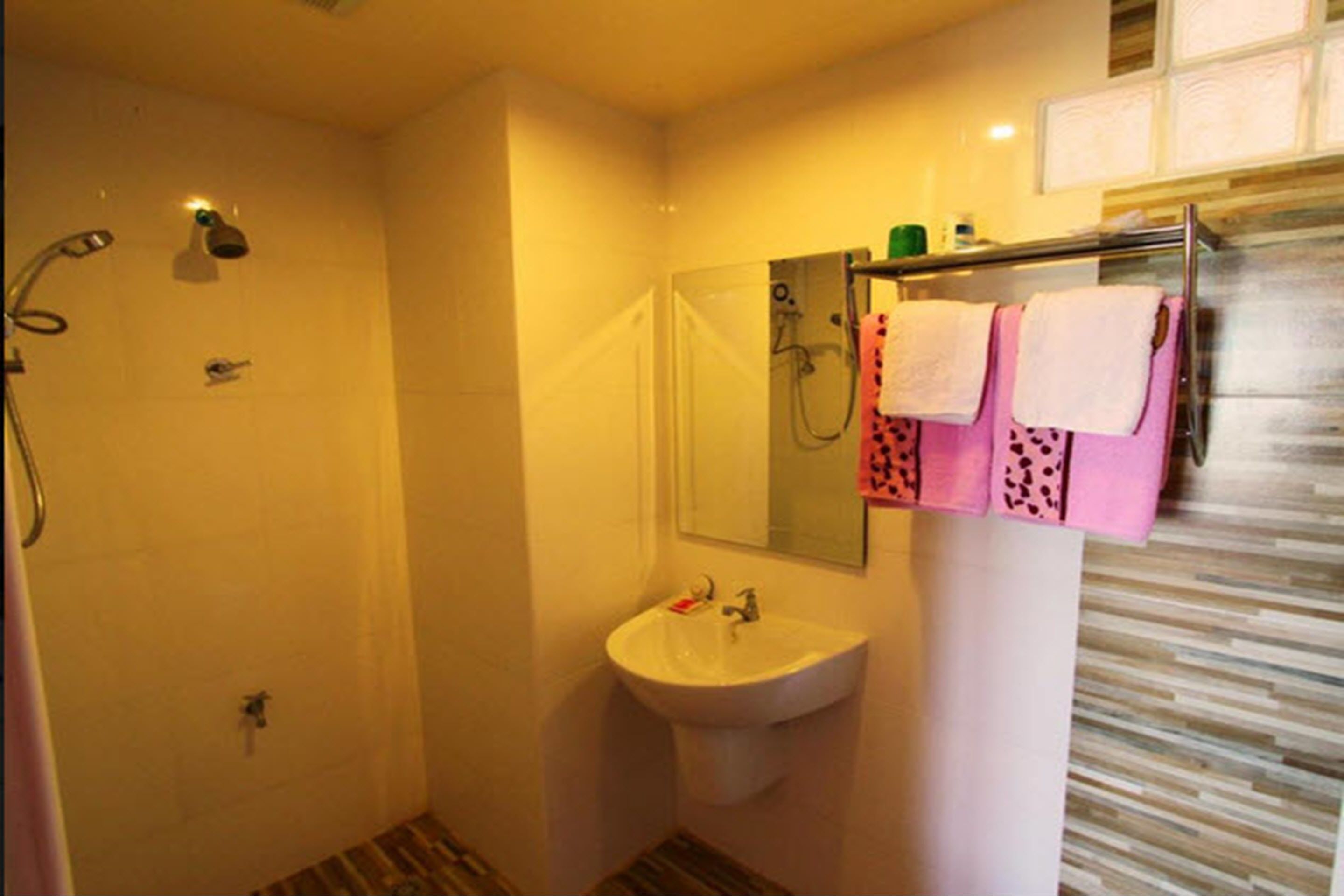 A small bathroom with a shower, sink, and a mirror. There are towels hanging on a rack.