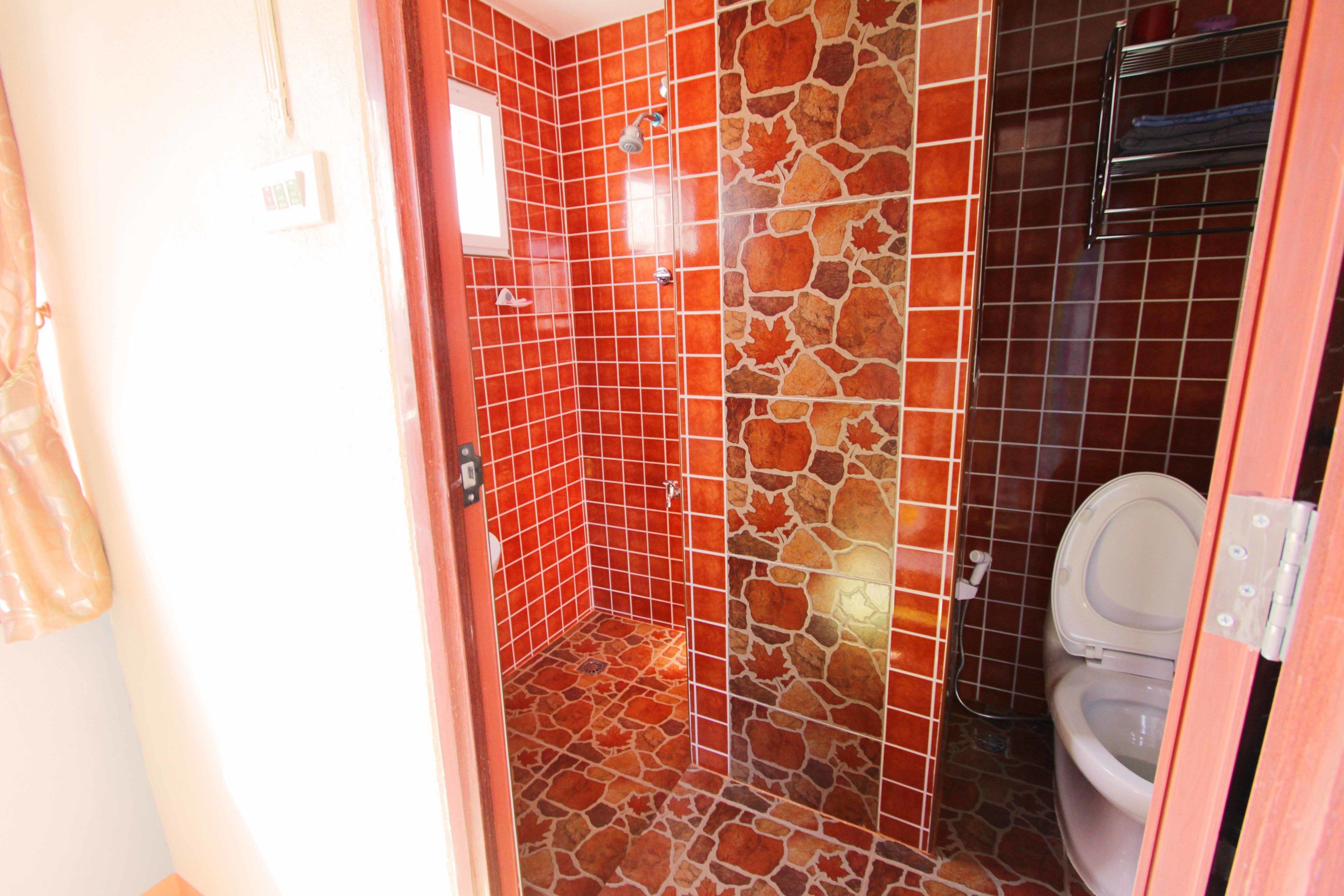 A bathroom with red and brown tiled walls, a shower area, and a toilet.