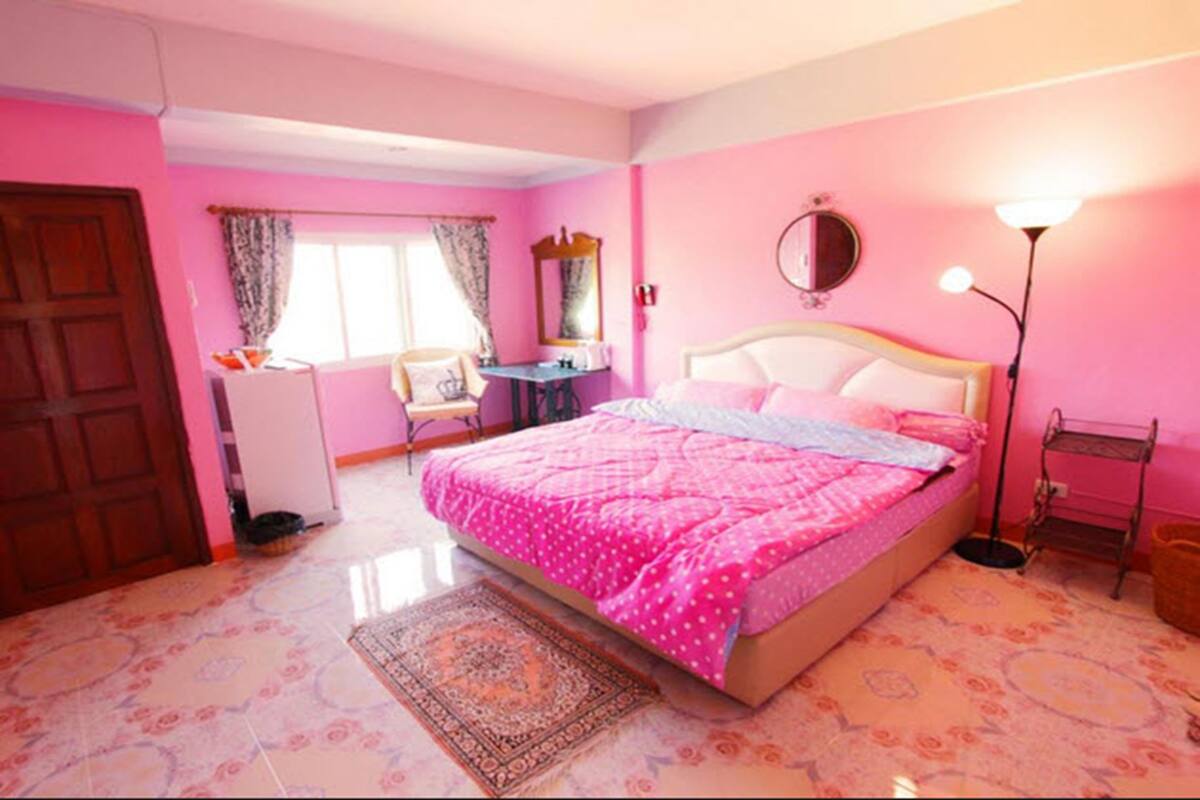 A pink-themed bedroom with a bed, a desk, a chair, a wardrobe, and a mirror.