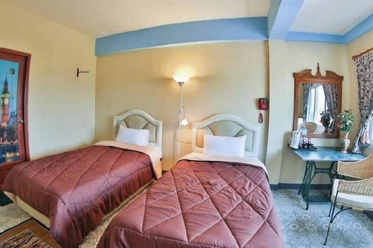 A hotel room with two beds, a desk, a chair, a lamp, and a mirror.