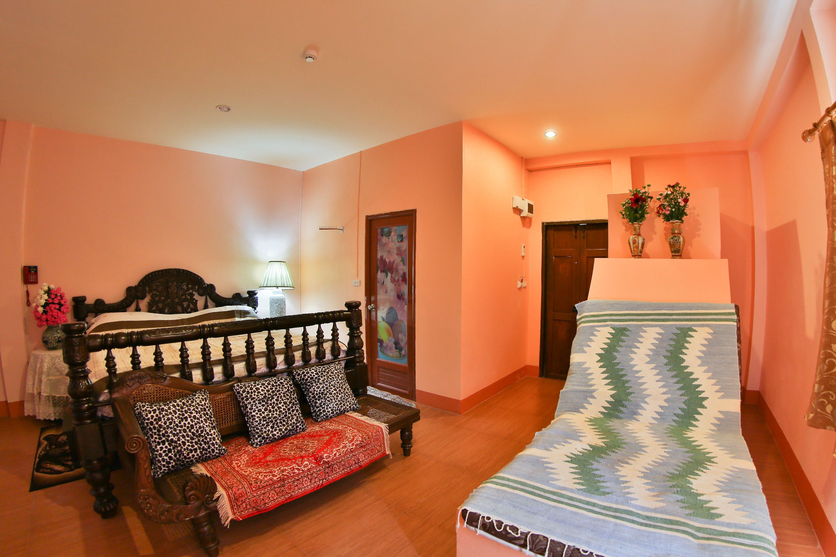 A bedroom with a wooden bed, a red and white patterned sofa, a small table, and a decorative rug.