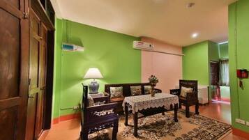A room with a green wall, a wooden door, a table with a lace tablecloth, a lamp, and a patterned rug.