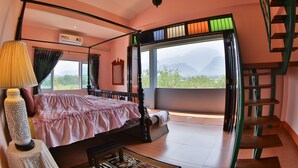 Ein Himmelbett mit Blick auf Berge durch große Fenster, eine Treppe und ein Tisch mit einer Lampe.