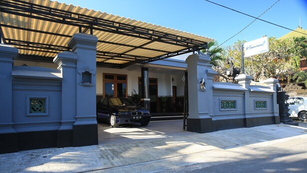 A gated entrance with a covered driveway, a parked car, and a building with traditional architectural features. - Puri Kusuma Guest House (Tabanan)