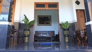 A hotel entrance with a tiled floor, two potted plants, a bench, and a door. - Puri Kusuma Guest House (Tabanan)