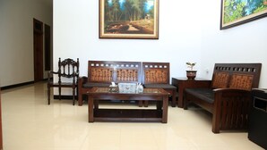 A room with a wooden coffee table, two sofas, and a chair. There are two framed paintings on the wall. - Puri Kusuma Guest House (Tabanan)
