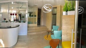 A modern interior with a curved reception desk, a staircase leading to an upper level, and a seating area with a small table and chairs. - Beach View Apartments And Studio (Tel Aviv)