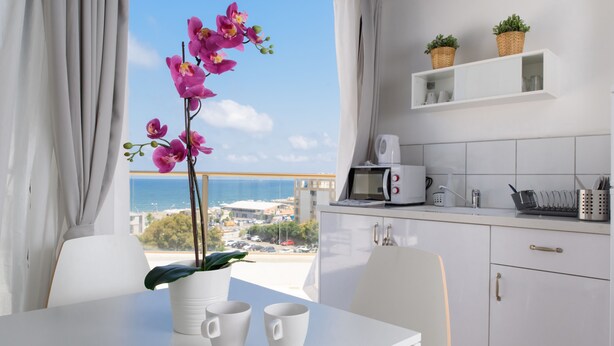 A modern kitchen with white cabinets, a white countertop, and a view of the sea. - Beach View Apartments And Studio (Tel Aviv)