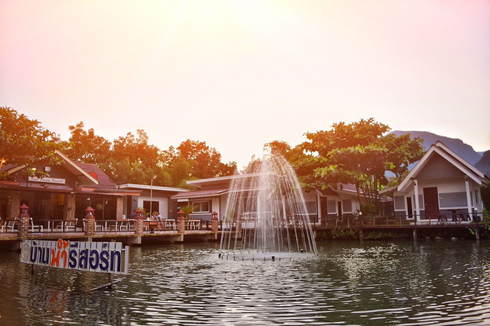 A hotel with a water fountain in the foreground, a signboard, and a view of the surrounding area.
