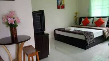 Una habitación de hotel con cama, televisión, una mesita con una silla y un florero.