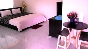 Une chambre à coucher comprenant un lit, un bureau, une chaise, une petite table avec un vase de fleurs et une fenêtre avec des rideaux.