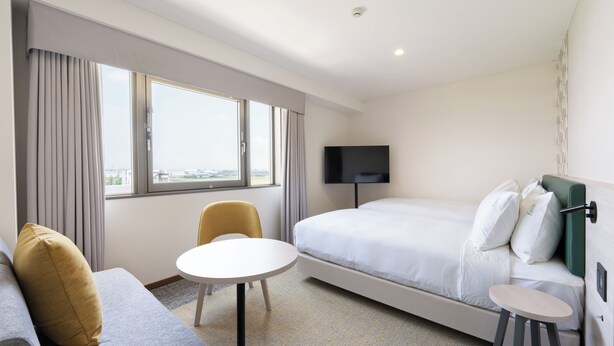 Una habitación de hotel con una cama, televisión, sofá, sillón y una mesita.