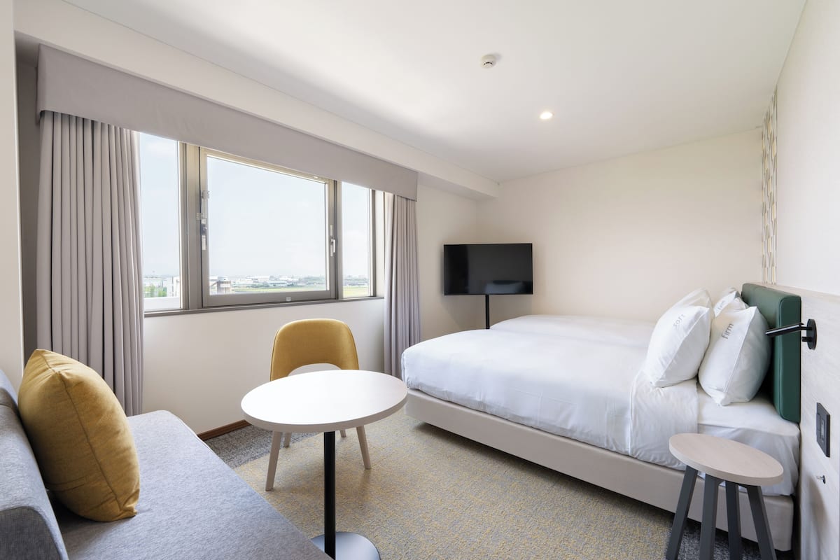 Una habitación de hotel con una cama, televisión, sofá, sillón y una mesita.