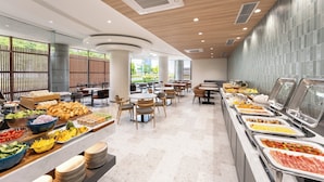 A buffet area with various food options, seating arrangements, and a view of greenery outside. - ANA Holiday Inn Tosu by IHG   (Tosu)