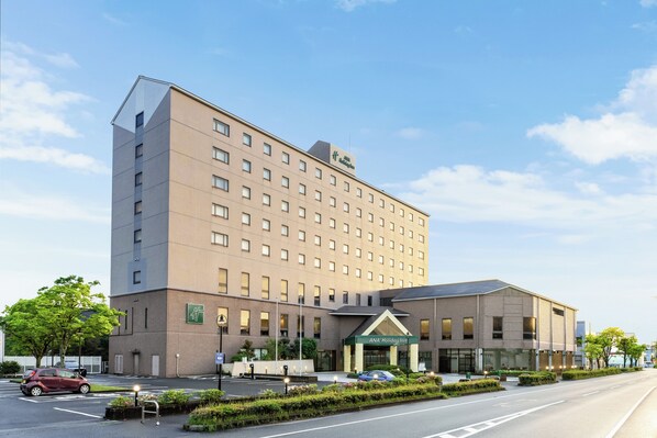 A multi-story hotel with a flat facade, a prominent entrance with a green awning, and a parking lot with cars.