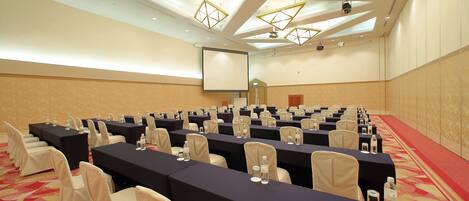A conference room with tables, chairs, and a projector screen.