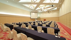 Un salón de conferencias con mesas, sillas y una pantalla para proyector.