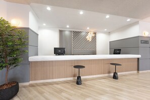 A reception desk with a wooden panel design, two bar stools, a potted plant, and a sign indicating a restroom. - ANA Holiday Inn Tosu by IHG   (Tosu)