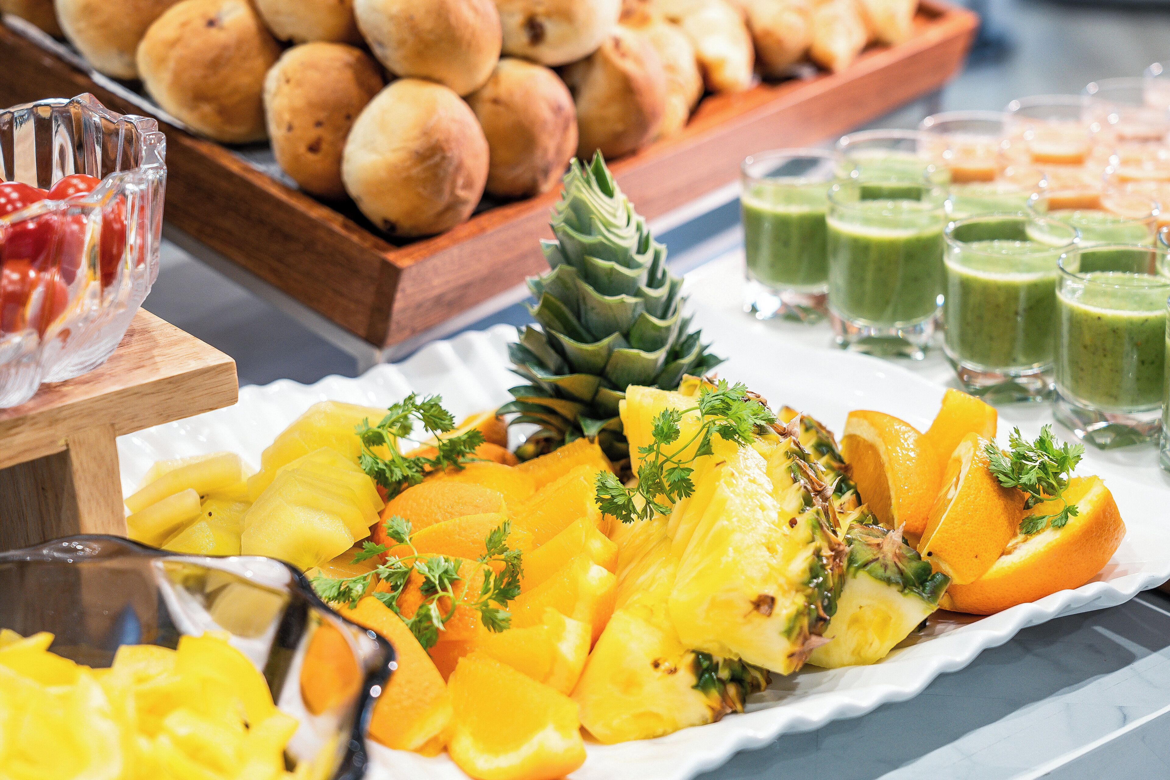 A buffet with a variety of fruits, including pineapple and orange slices, and a selection of bread and green smoothies.