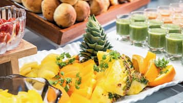 A buffet with a variety of fruits, including pineapple and orange slices, and a selection of bread and green smoothies.