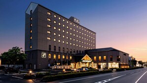 Un hotel de varios pisos con un llamativo letrero de ANA Holiday Inn, un estacionamiento y una entrada bien iluminada.