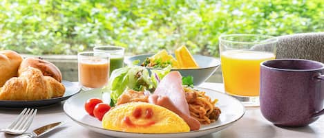 A breakfast setting with croissants, a plate of food, a glass of orange juice, and a purple mug on a table.