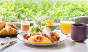 Un desayuno con cruasanes, un plato de comida, un vaso de jugo de naranja y una taza morada sobre una mesa.