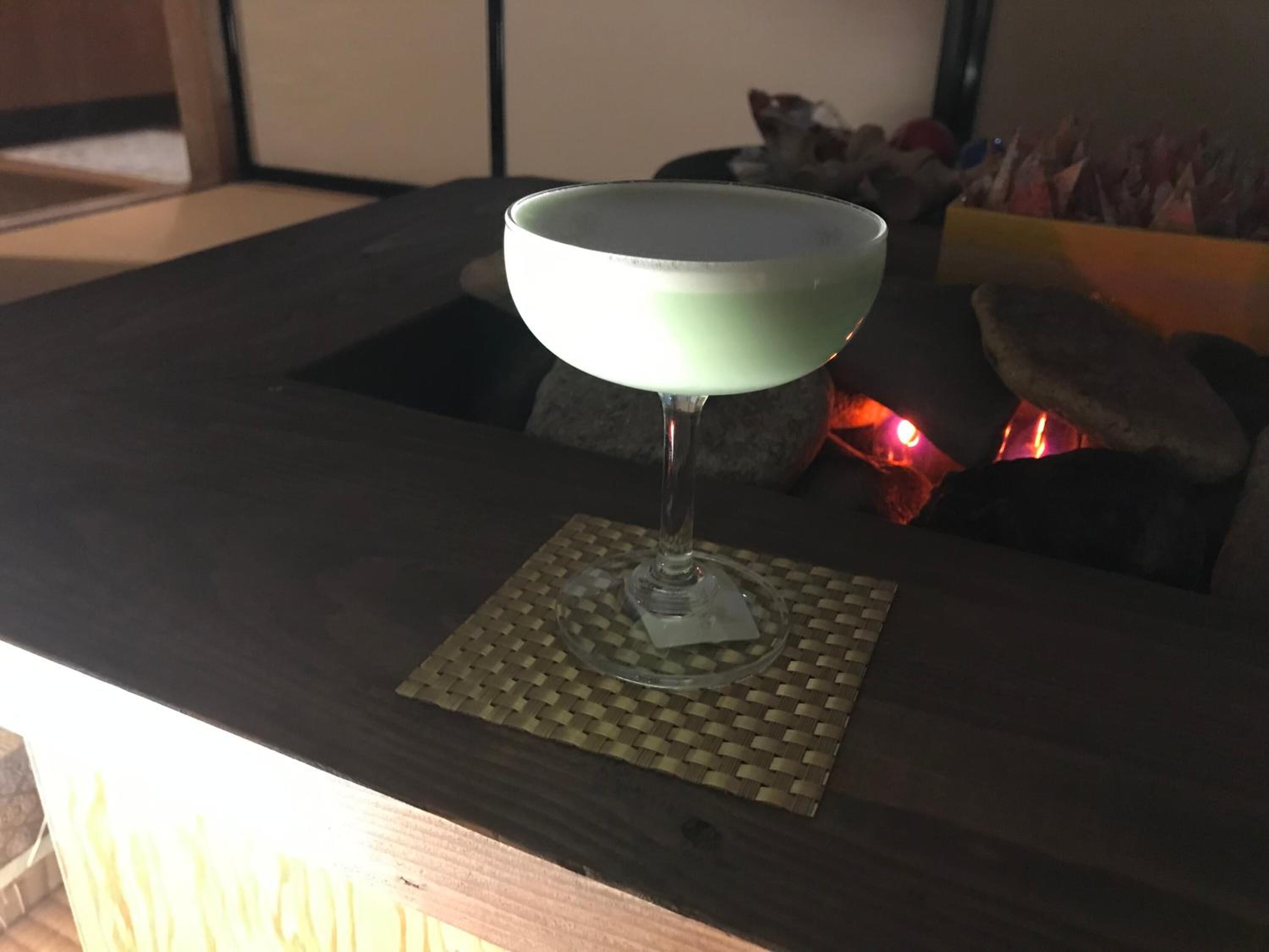 A cocktail glass on a coaster with a woven mat underneath, placed on a dark wooden table.