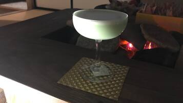 A cocktail glass on a coaster with a woven mat underneath, placed on a dark wooden table.