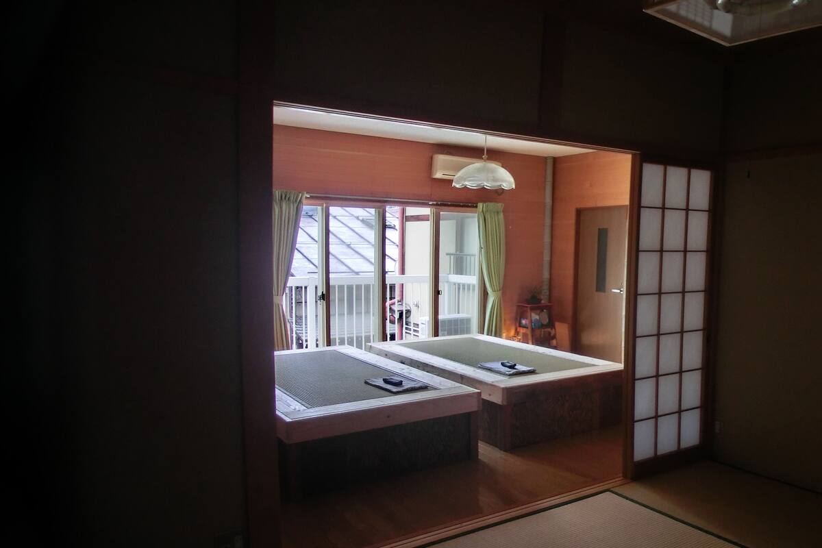 A traditional Japanese room with tatami flooring, a low wooden table, and a sliding door leading to a balcony.