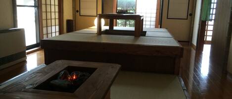 Una habitación japonesa tradicional con suelo de tatami, una mesa de madera baja con chimenea integrada y puertas correderas.