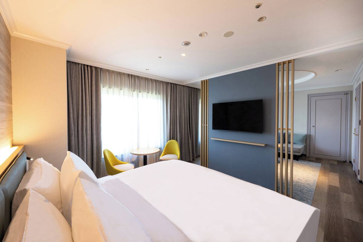 A hotel room with a large bed, a TV mounted on the wall, a small table, and a chair.