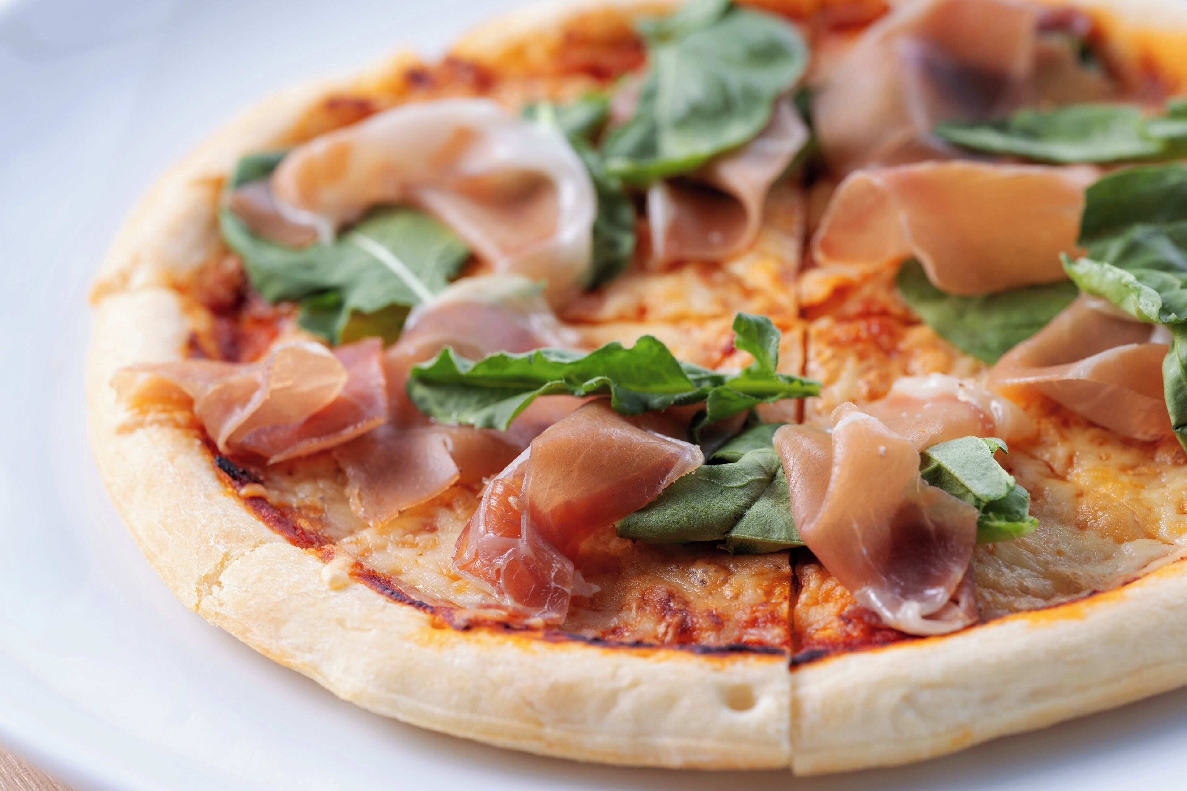 A pizza with prosciutto and spinach on a white plate.