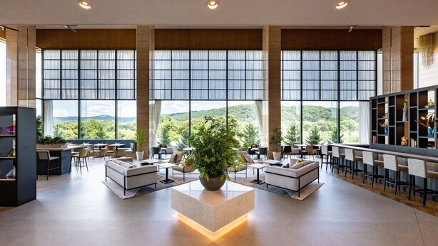 A spacious lobby with large windows offering a view of a mountainous landscape. There are seating areas with sofas and tables, and a bar area with stools. - ANA Holiday Inn Iwate Kitakami by IHG (Kitakami)