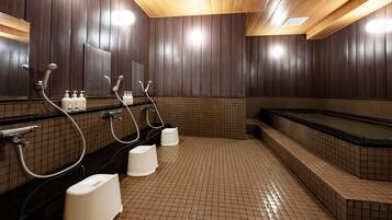 A public sauna with multiple showerheads, a large bathtub, and tiled flooring.