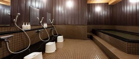 A public sauna with multiple showerheads, a large bathtub, and tiled flooring.