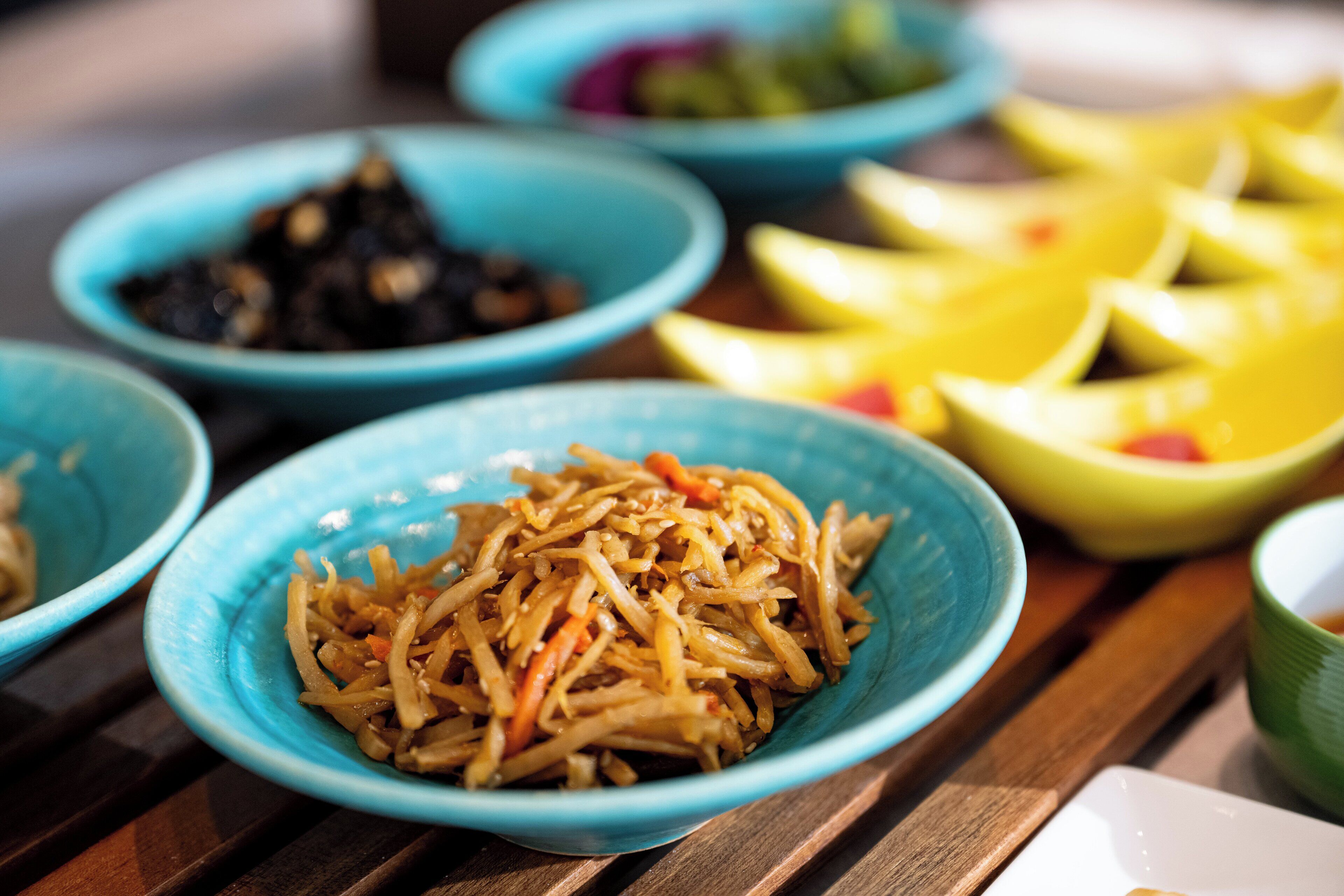 A table with various dishes in bowls, including noodles and sliced vegetables.