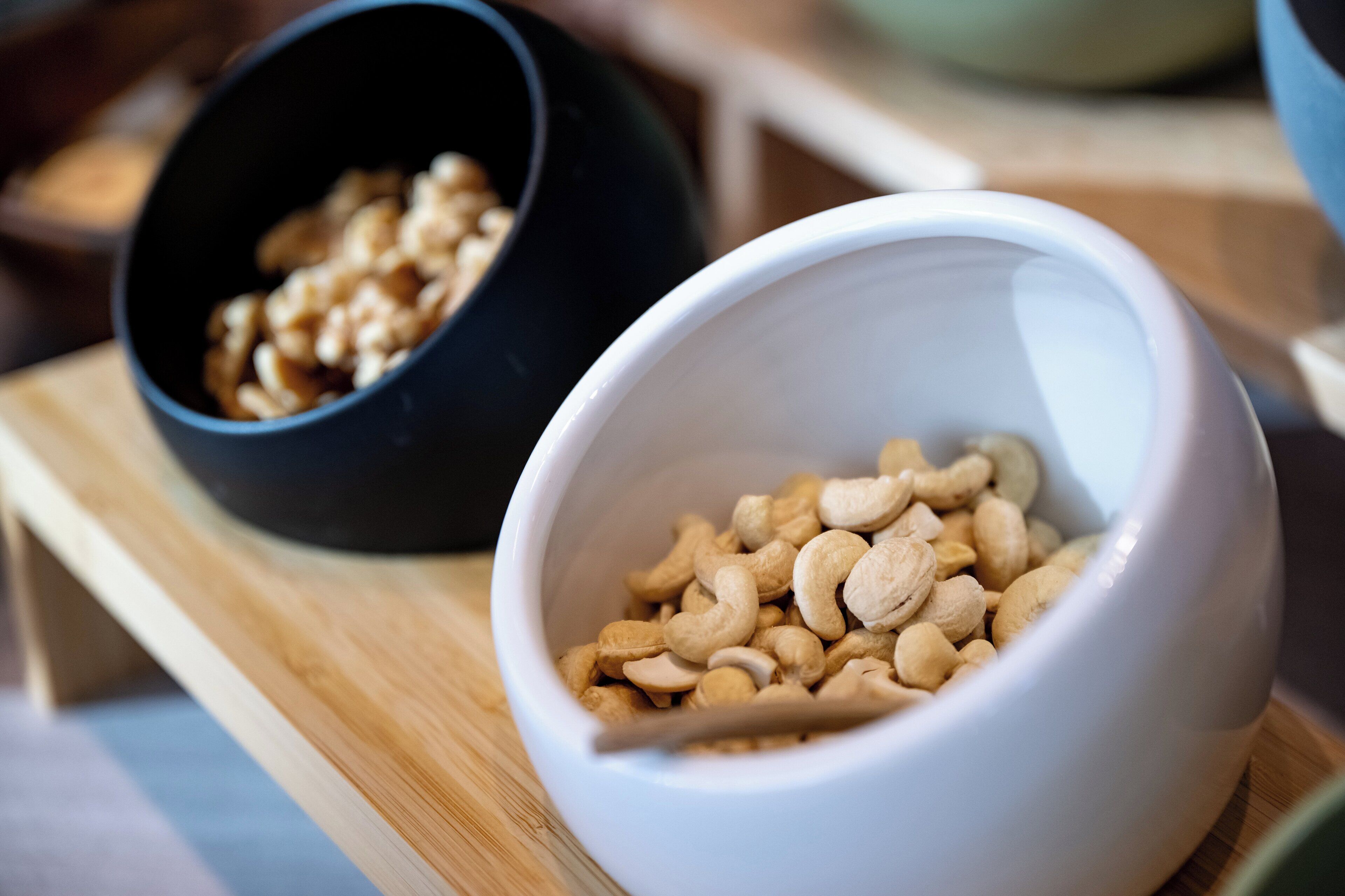 Two bowls on a wooden surface, one containing cashews and the other containing granola.
